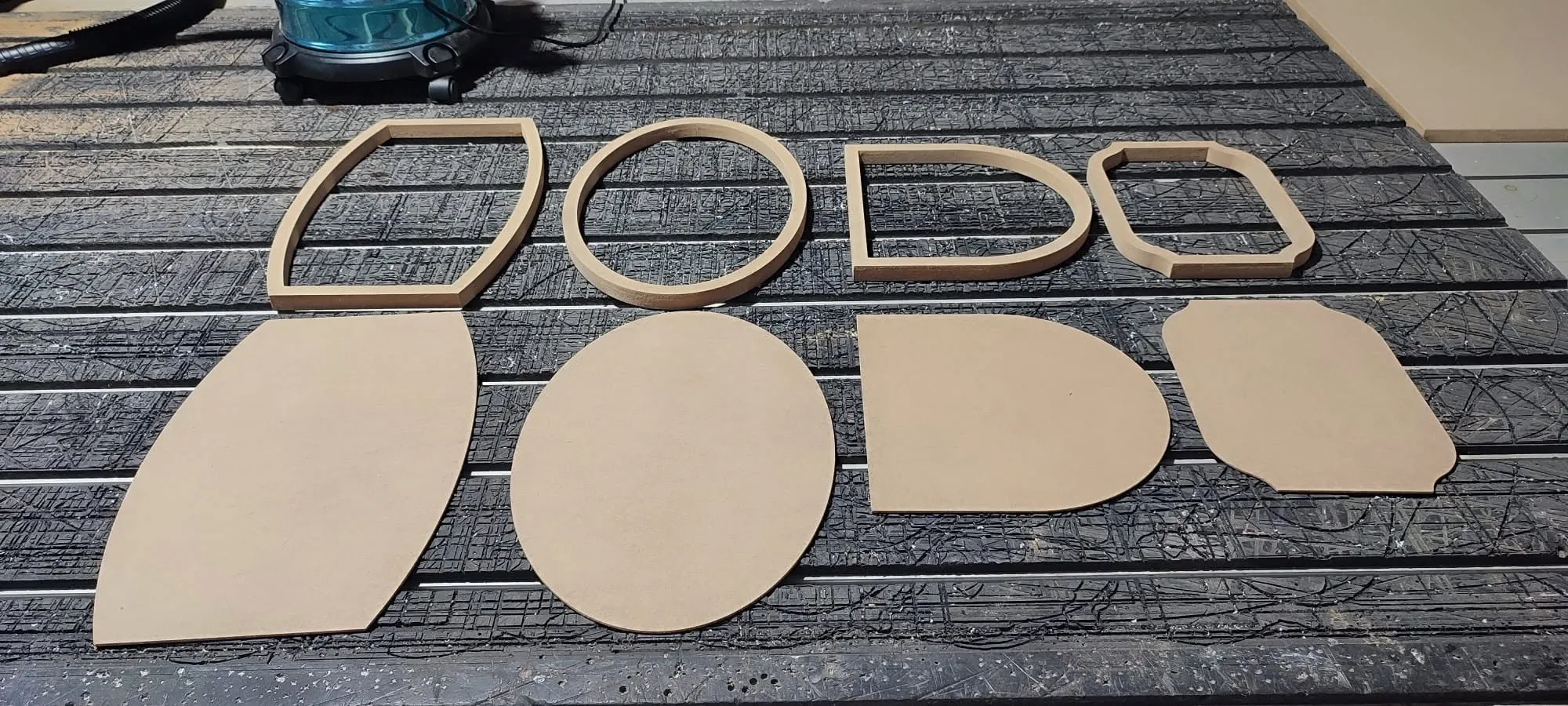 ชิ้นงานไม้ MDF ตัดขึ้นรูปหลายทรง ทั้งชิ้นเต็มและกรอบ วางบนโต๊ะเครื่อง CNC